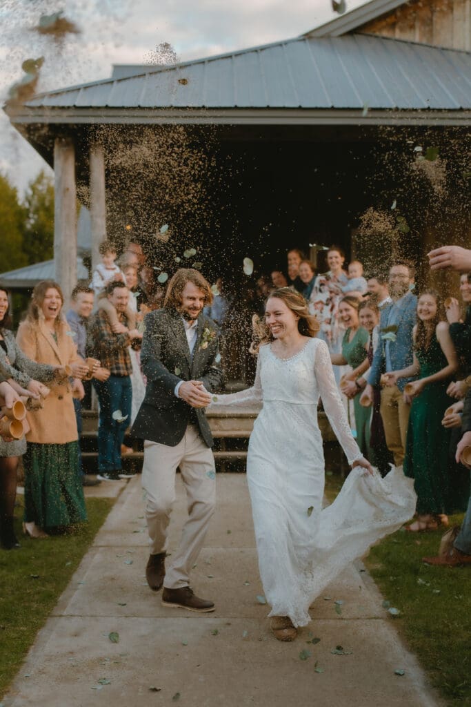 A bride and groom smiling and walking through lavender and flower petal toss reception exit in Markdale, Ontario at Campfire Bible Camp.