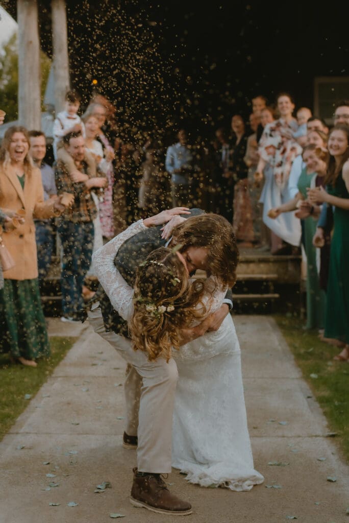 A bride and groom kissing and walking through guests as they toss lavender and flower petals at reception exit in Markdale, Ontario at Campfire Bible Camp.