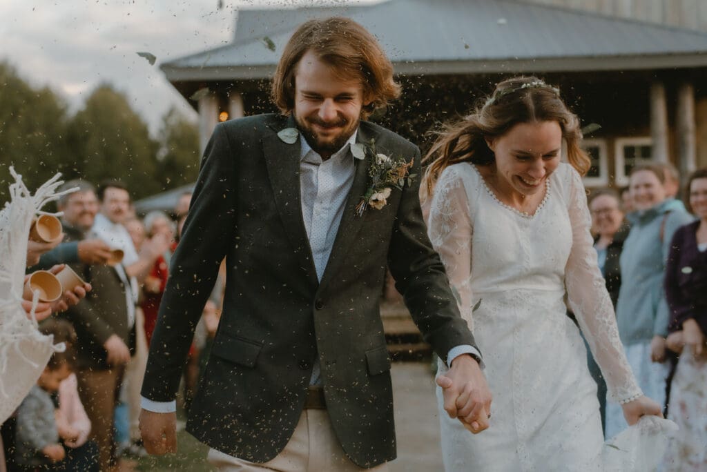 A bride and groom smiling and walking through guests as they toss lavender and flower petals at reception exit in Markdale, Ontario at Campfire Bible Camp.
