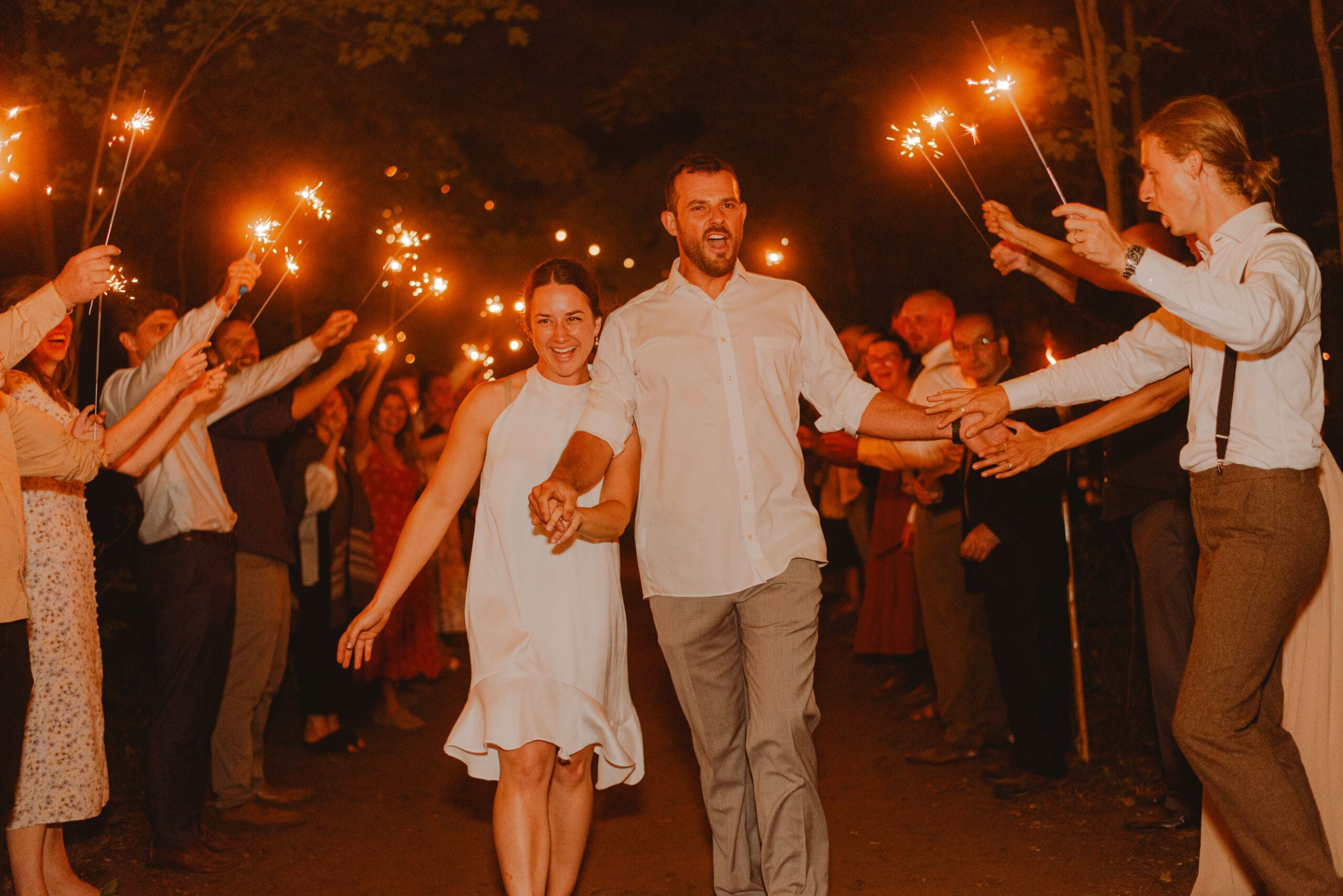 A bride and groom walking happily through sparkler exit at night smiling and giving high-fives in Stratford Ontario