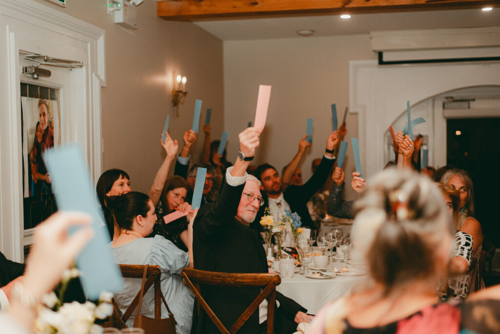Guests laughing and participating in the shoe game, raising strips of paper to guess in Ottawa's Strathmere Wedding Estate.