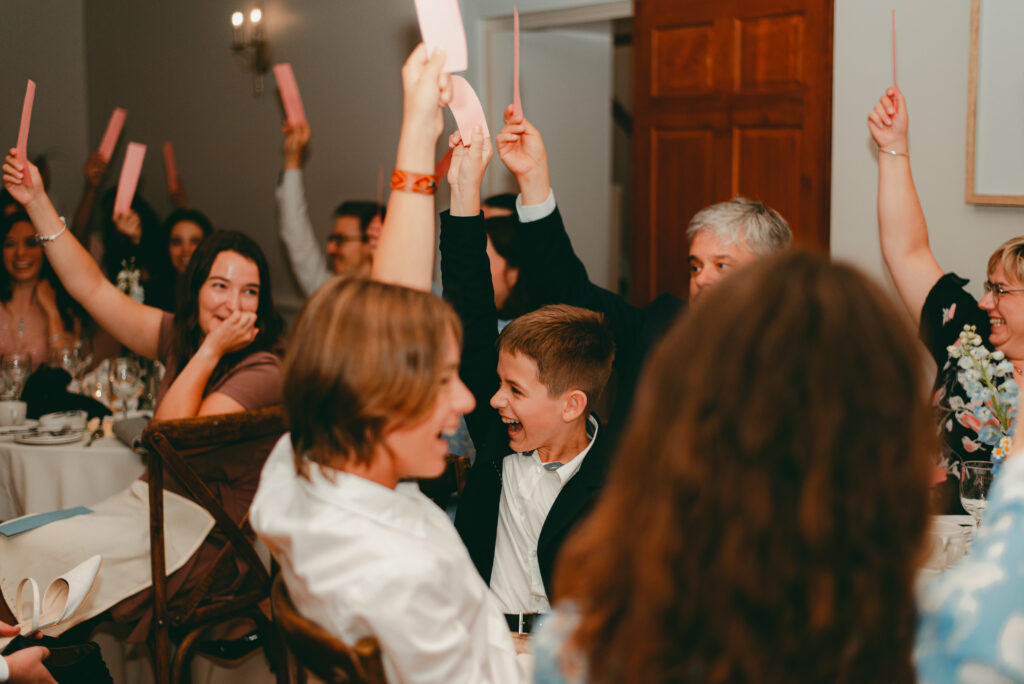 Guests laughing and participating in the shoe game, raising strips of paper to guess in Ottawa's Strathmere Wedding Estate.
