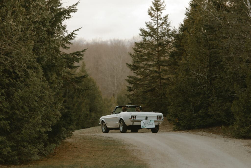 Bride and groom waving goodbye to guests as they drive away into forest in Markdale, Ontario at Campfire Bible Camp.