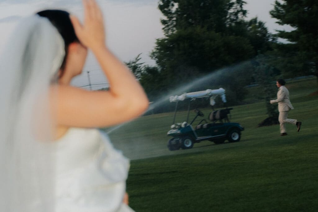 Bride reacting to groom running to get golf course during unexpected sprinklers during a sunset wedding portrait session in Hamilton.