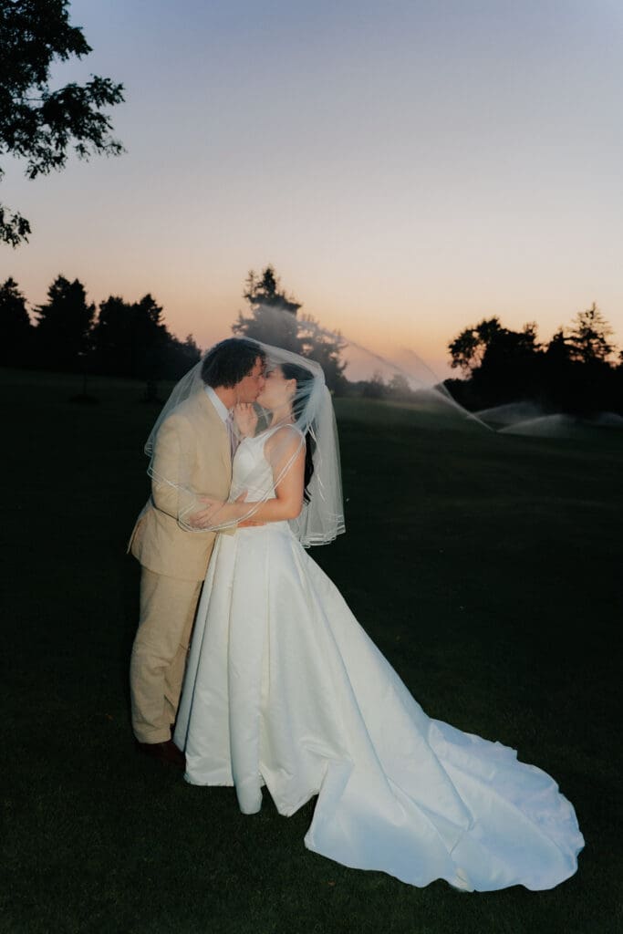 Romantic wedding couple kissing at sunset with backlit water spray from sprinklers creating a dreamlike atmosphere, Hamilton Ontario.