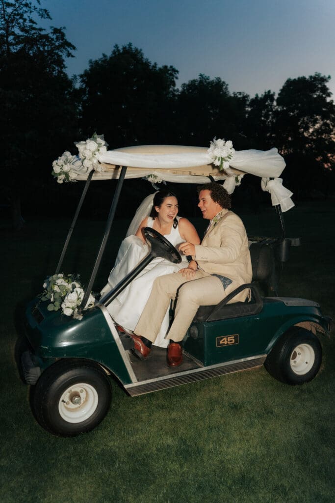 Groom driving a golf cart through water sprinklers with his bride laughing beside him during sunset portraits at Buncrana Golf Club.