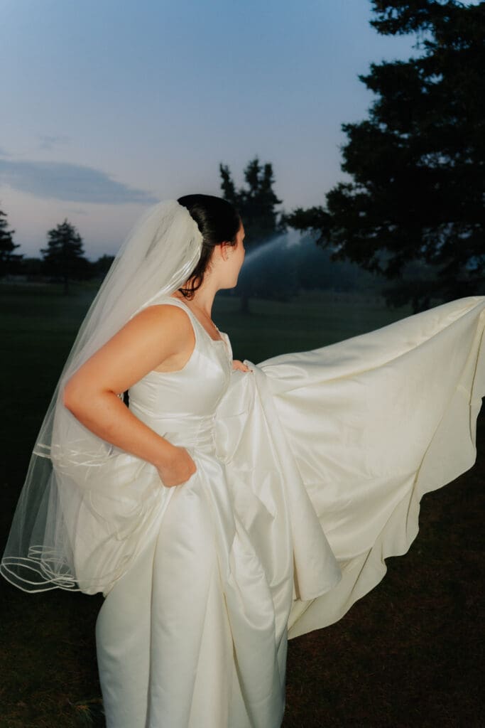 Side profile of bride in a classic satin wedding dress as golf course sprinklers begin to spray in the background at Buncrana Golf Course.