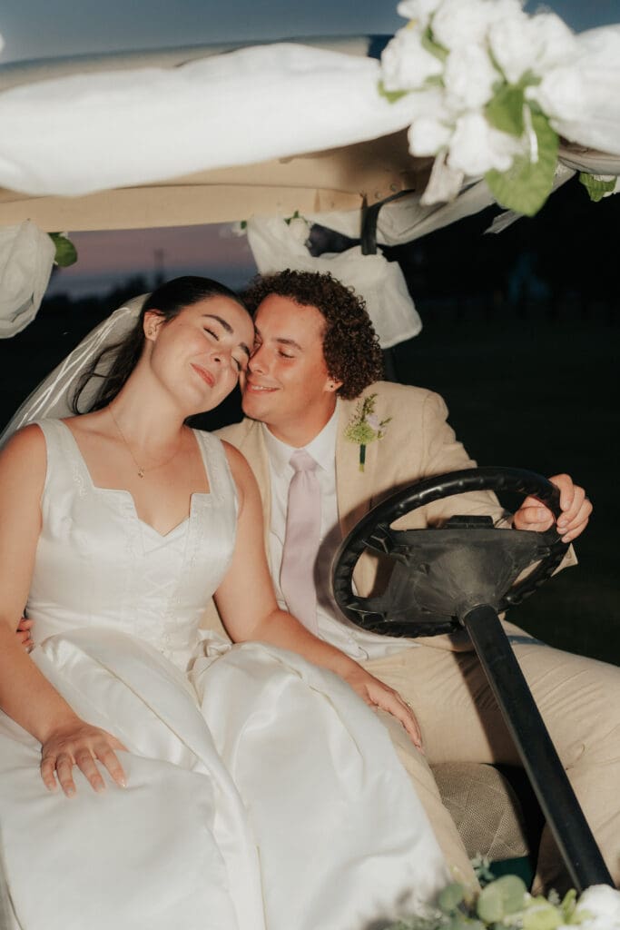 Close-up intimate moment of a bride and groom cuddling on a golf cart at dusk, showing authentic emotion and joy after their wedding ceremony.