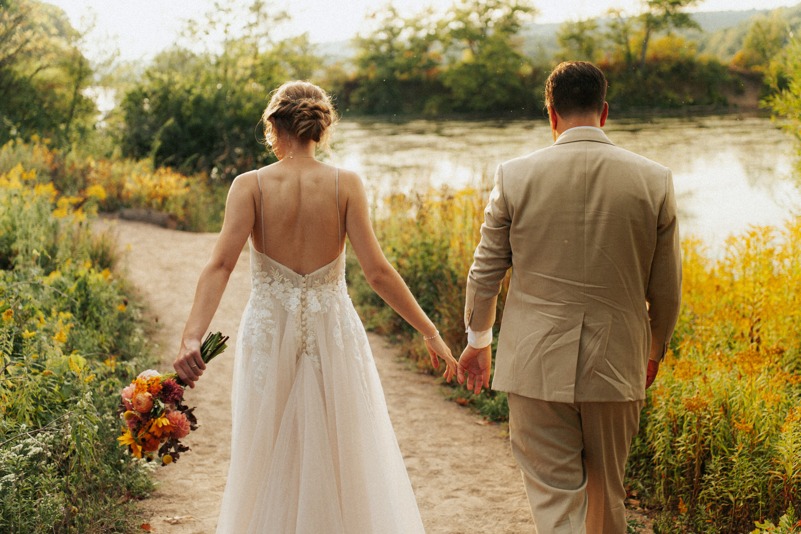 Bride and groom walking away holding hands and wild flower bouquet at fall wedding at Princess Point Hamilton.