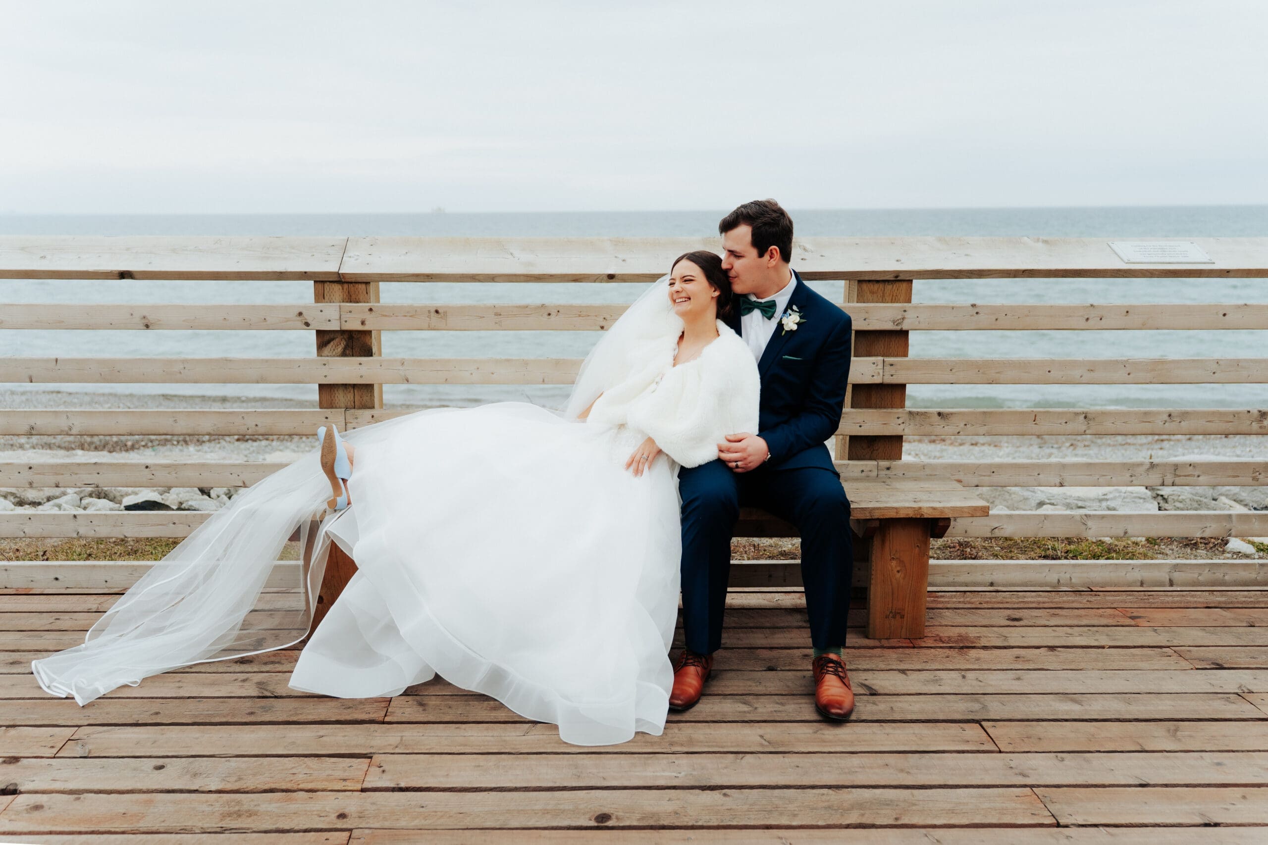 Bride and groom sitting on bench in front of Lake Ontario at Lakeview by Carmens in Hamilton.