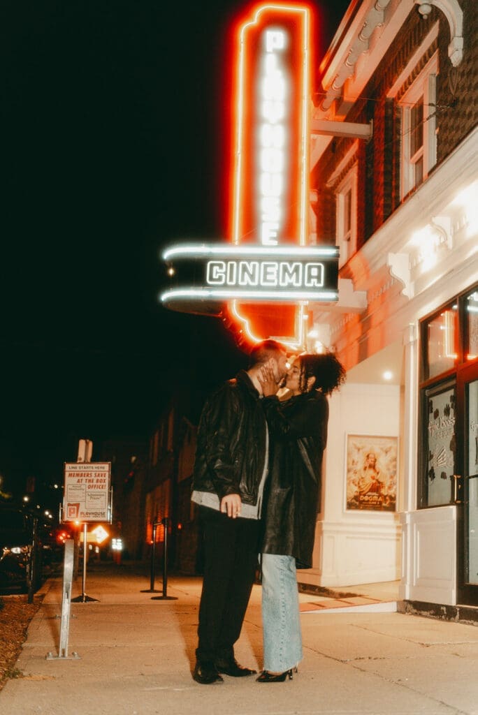 Couple kissing wearing black leather in front of Playhouse cinema vintage movie theatre. Hamilton wedding photographer.